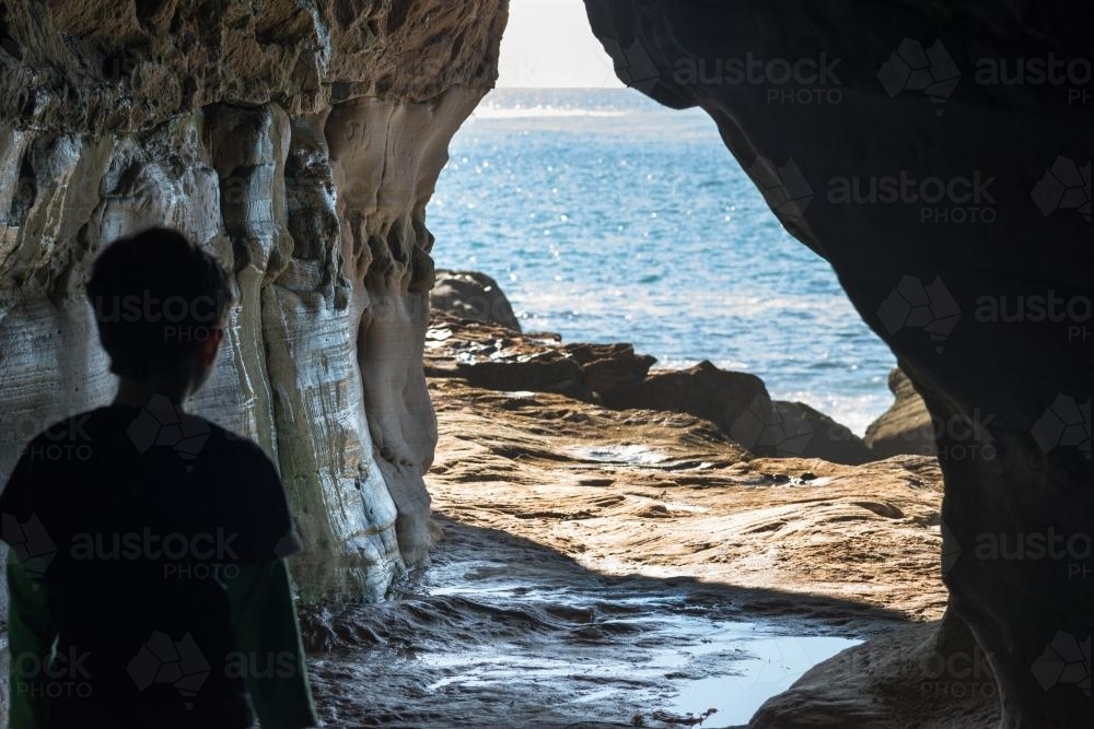 Child walking out through rock tunnel near ocean - Australian Stock Image