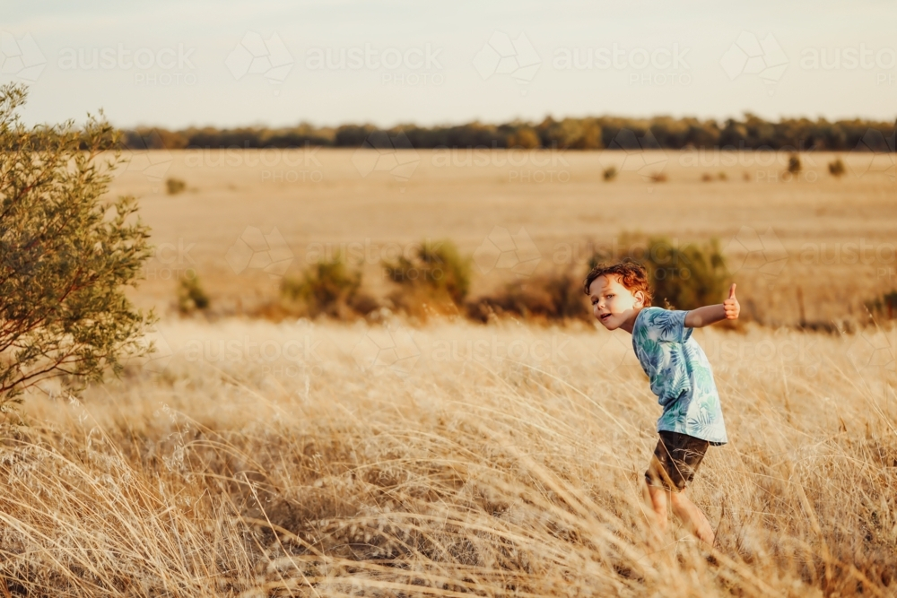 Child walking through long dry grass in golden afternoon light - Australian Stock Image
