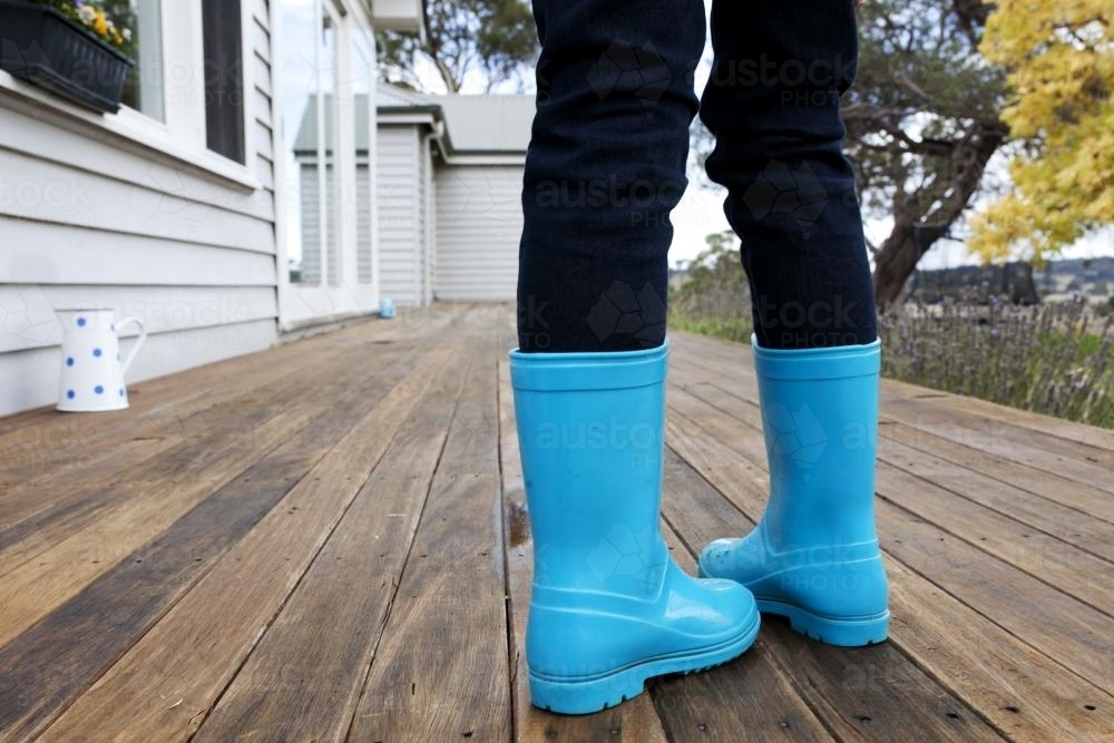 Child wearing blue gumboots on wooden verandah - Australian Stock Image