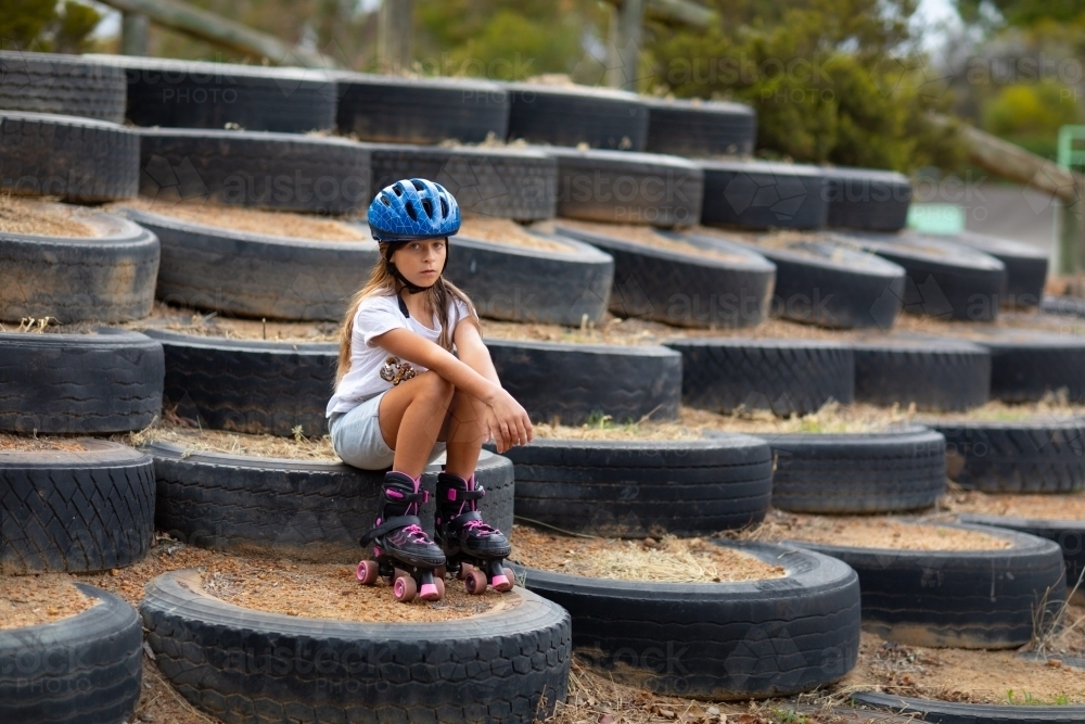 Child wearing blue helmet and roller skates sitting resting - Australian Stock Image