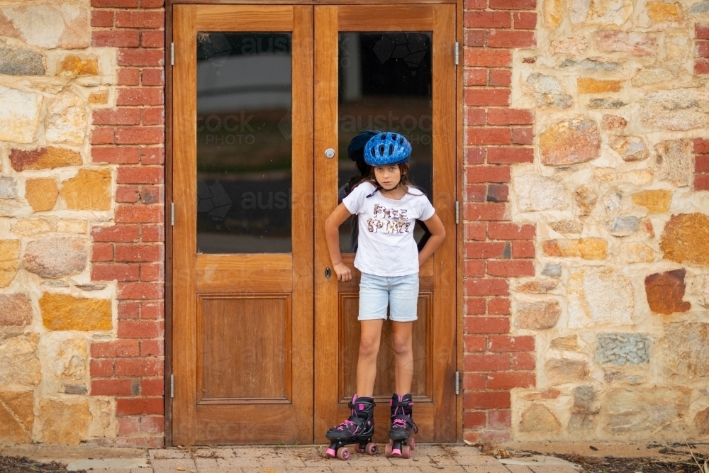 child wearing roller skates and helmet standing in front of doors - Australian Stock Image