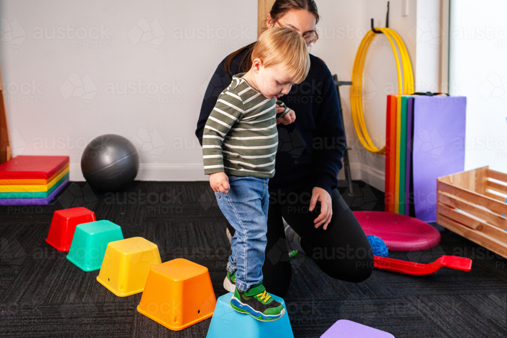 Child with female physio walking on coloured blocks working on balance - Australian Stock Image