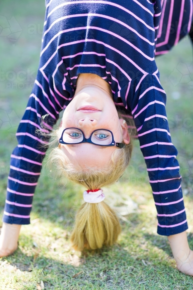Child with glasses and ponytail doing a bend back on grass - Australian Stock Image
