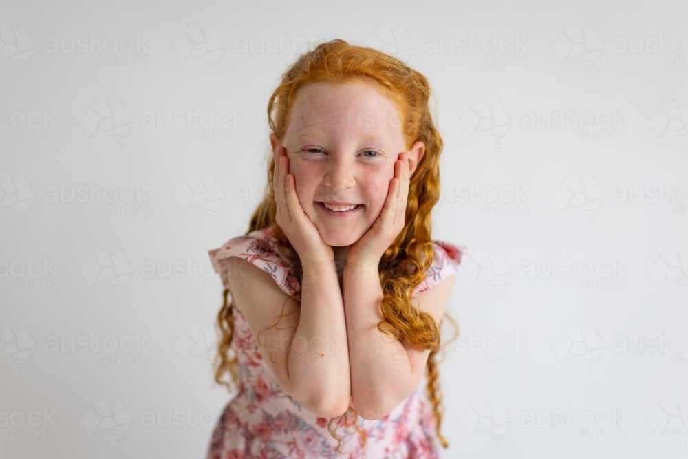 child with hands to face looking at camera against plain white background - Australian Stock Image