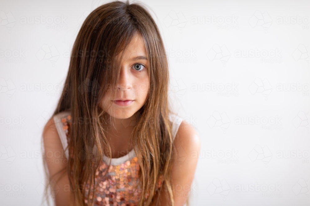 child with long hair  over face revealing one eye on plain background - Australian Stock Image