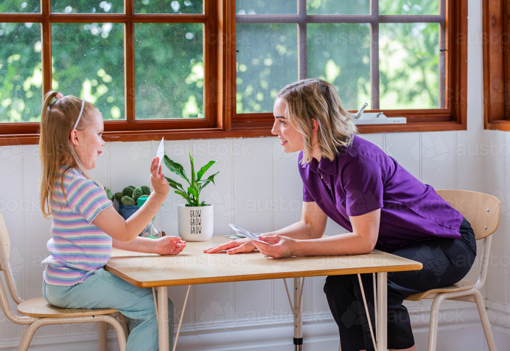 Child with speech disability looking at sound cards talking with speech-language pathologist - Australian Stock Image