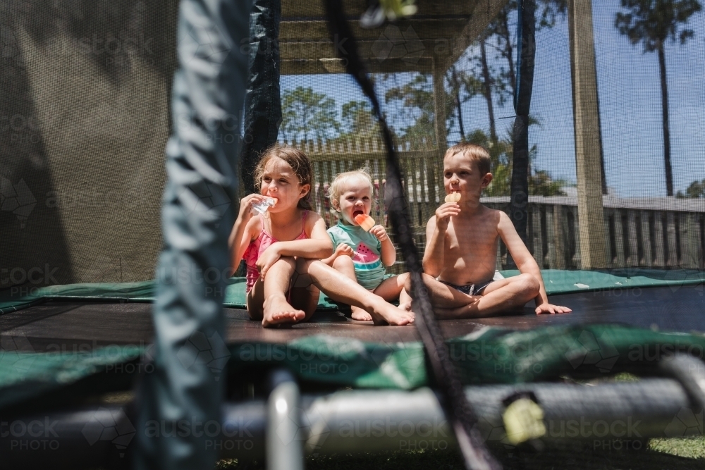 Children eating ice blocks on a trampoline - Australian Stock Image
