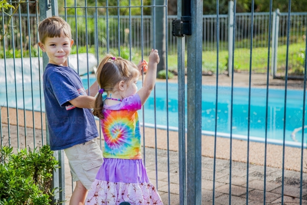 Children holding fence bars looking into pool yard - Australian Stock Image