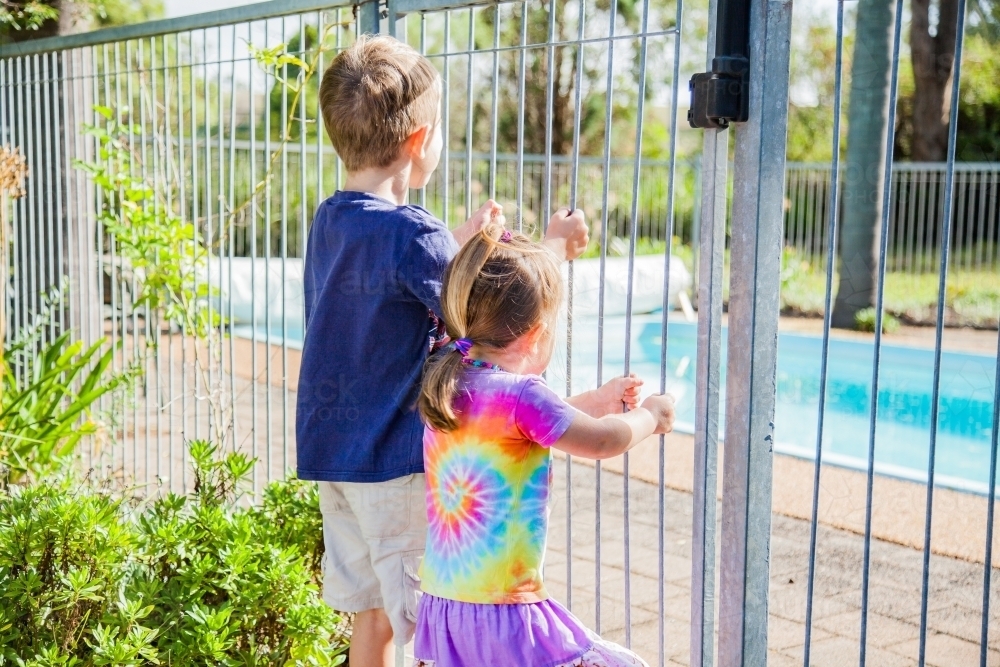 Children holding fence bars looking into pool yard - Australian Stock Image