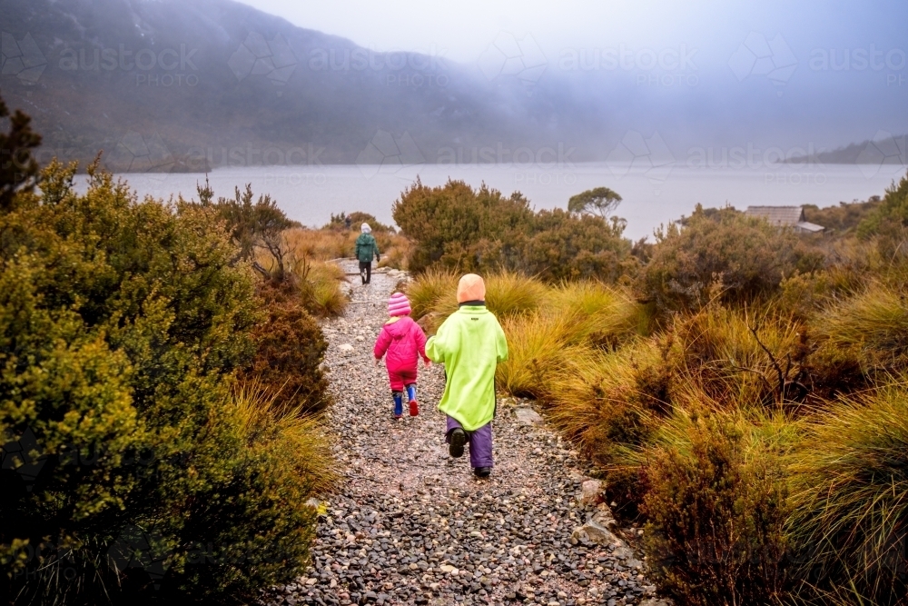 Children in bright rain jackets running down path on overcast day - Australian Stock Image