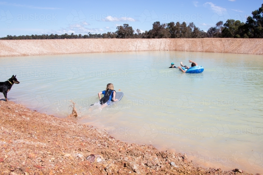 Children playing in a farm dam, watched by a dog - Australian Stock Image