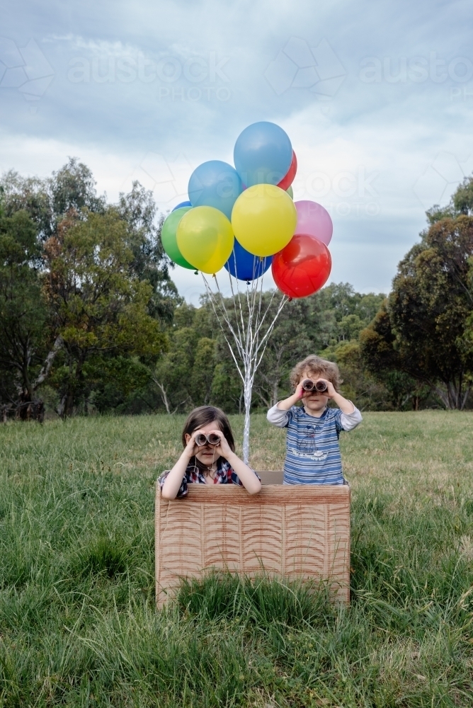 Children play in hot air balloon made from a box & balloons, looking through toilet roll binoculars - Australian Stock Image