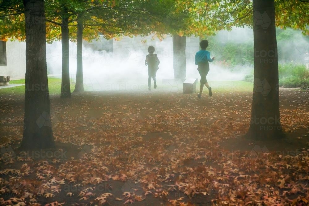 Children running into fog in a forest. - Australian Stock Image