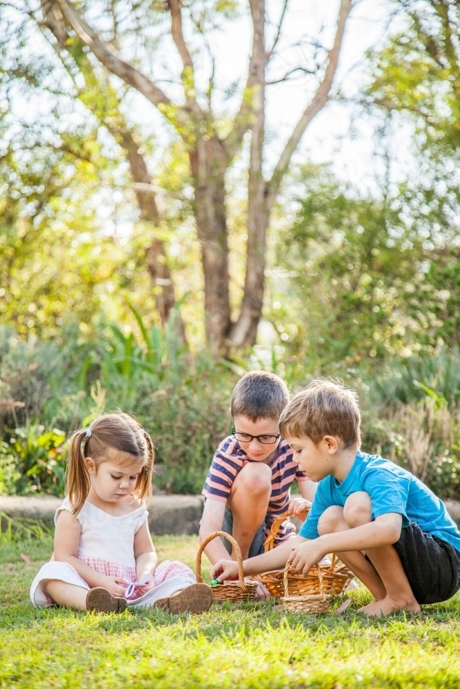 Children sitting on grass sorting out baskets of Easter eggs - Australian Stock Image