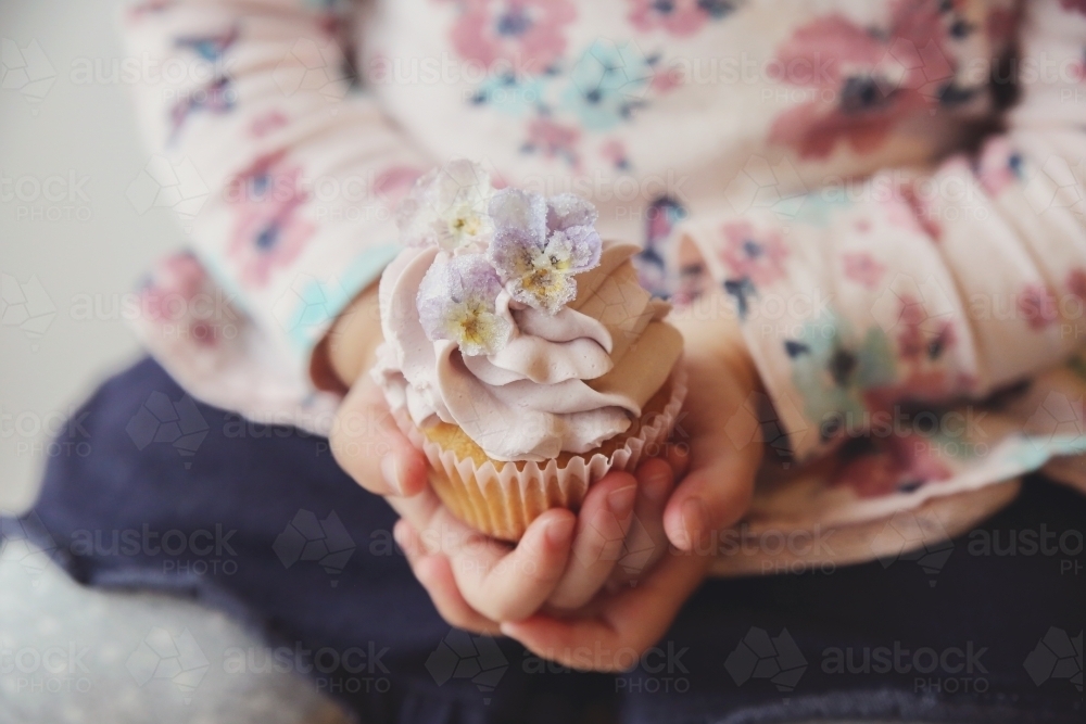 Childs hands holding purple flower cupcake - Australian Stock Image