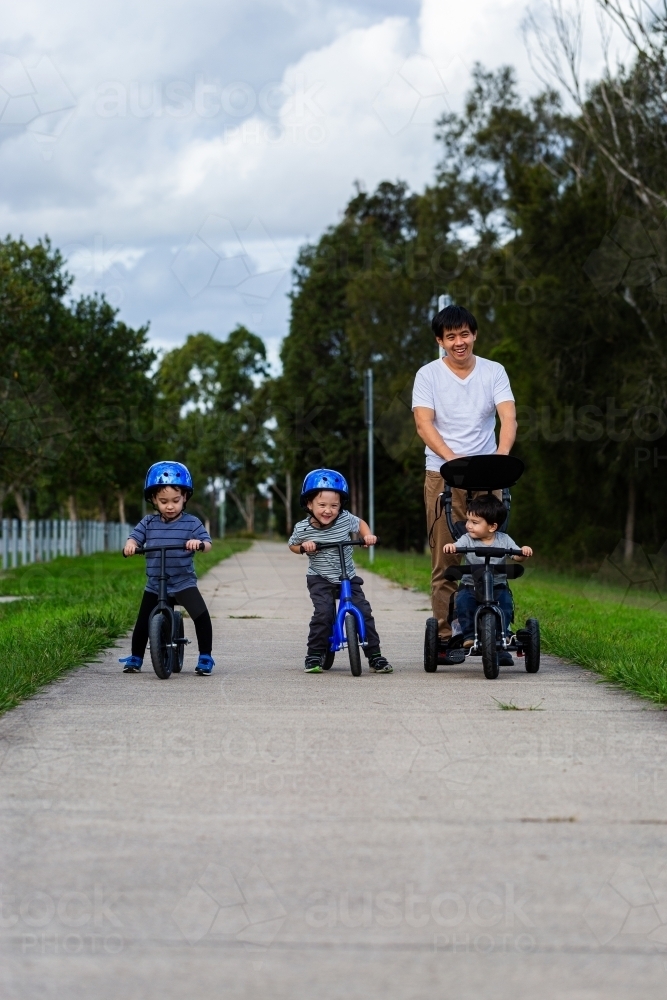 Chinese australian dad on walk with his sons riding balance bikes on footpath - Australian Stock Image