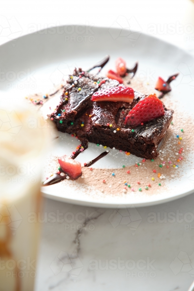 chocolate brownie with sprinkles and strawberry toppings on a white plate - Australian Stock Image