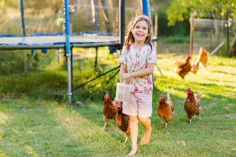 Chooks following country kid around farm in afternoon light - Australian Stock Image
