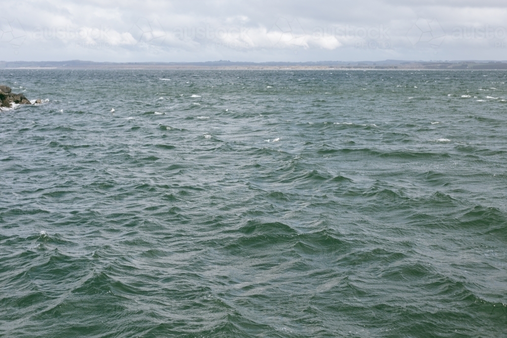 Choppy waves with land along the horizon and clouds in sky - Australian Stock Image