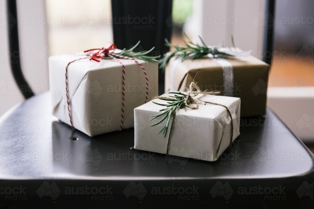 Christmas gifts in neutral wrapping sitting on a dining chair - Australian Stock Image