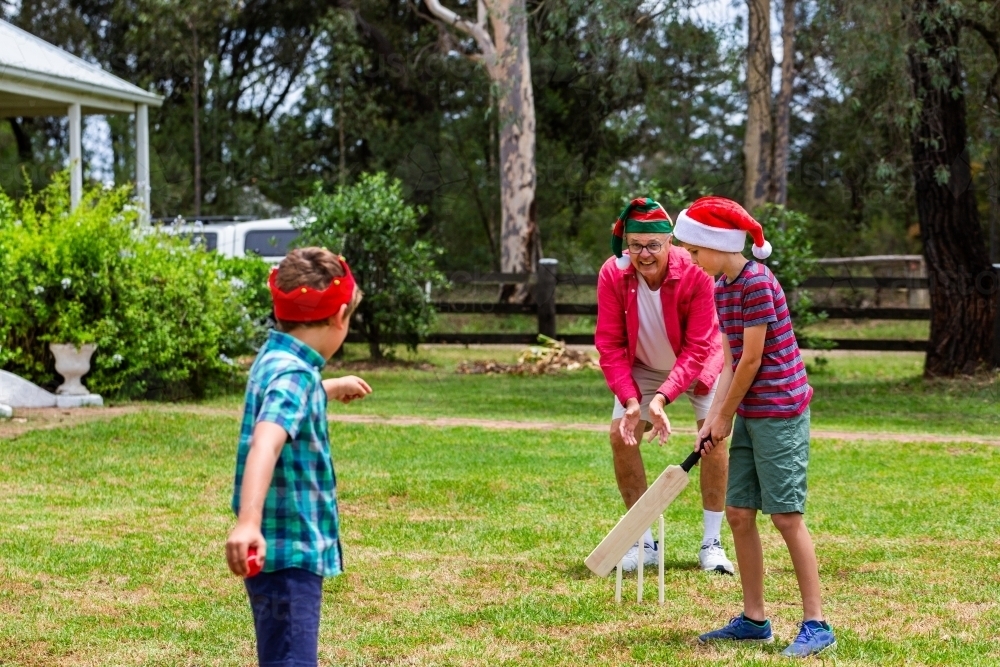 Christmastime backyard cricket game two young aussie boys playing with grandfather - Australian Stock Image