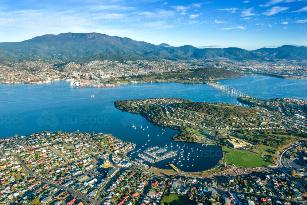 City sprawling around a wide blue harbour beneath green mountains. - Australian Stock Image