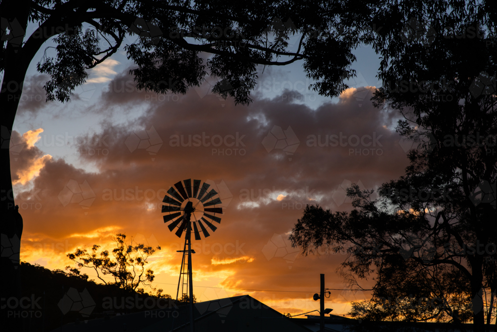 Classic windmill stands tall in silhouette at sunset - Australian Stock Image