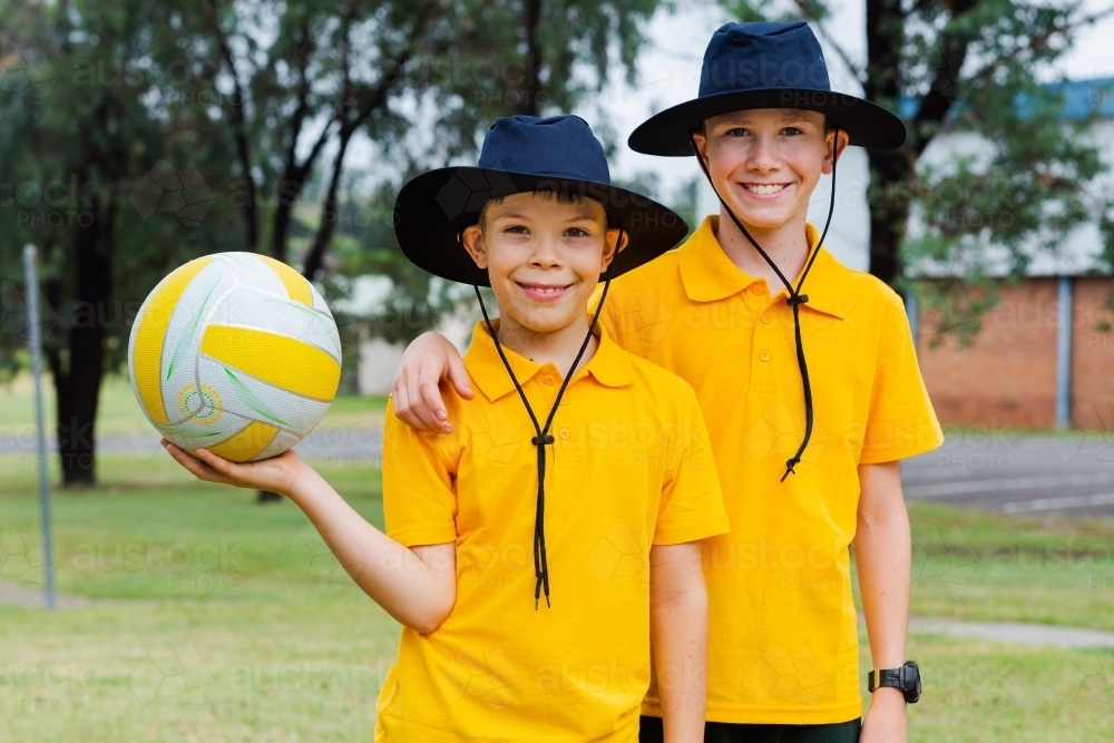 Classmates standing outside in the playground with hats on and a ball - Australian Stock Image