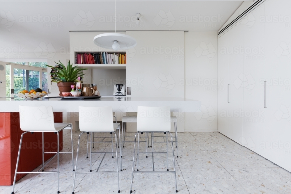 Clean crisp white modern kitchen island bench with high chairs and terrazzo floor - Australian Stock Image