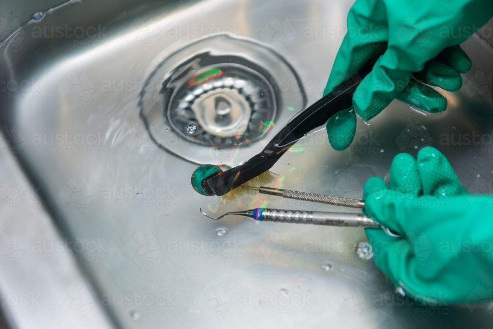 Cleaning dental instruments by hand in sink - Australian Stock Image