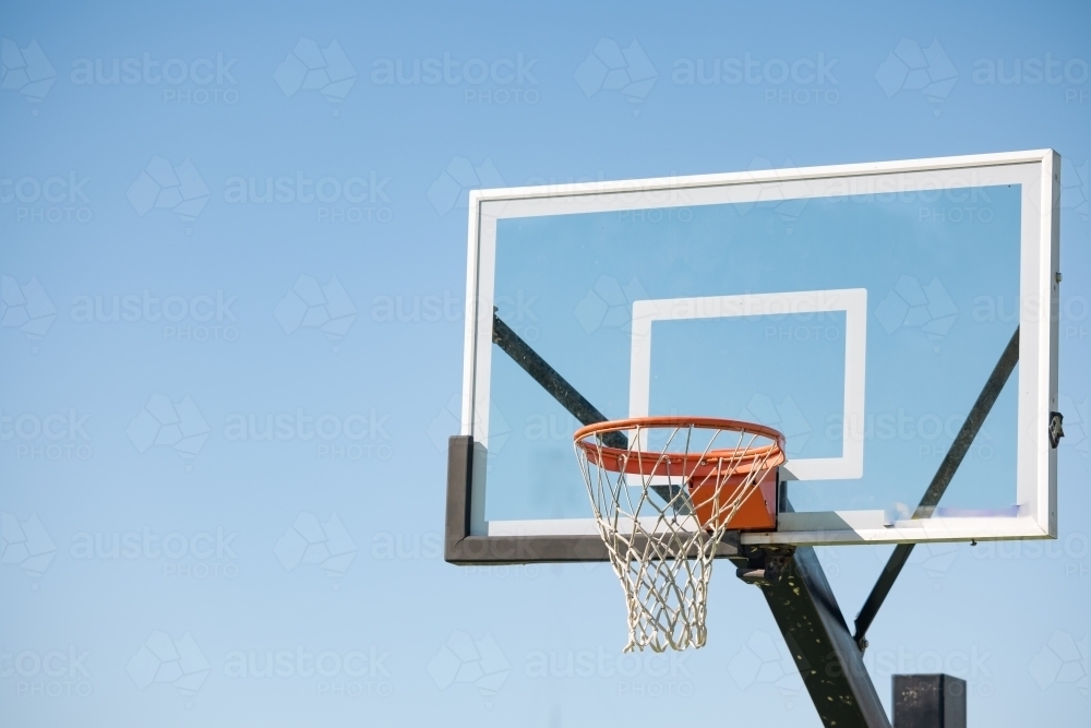 Clear glass basketball backboard with rim on blue sky background with copy space - Australian Stock Image
