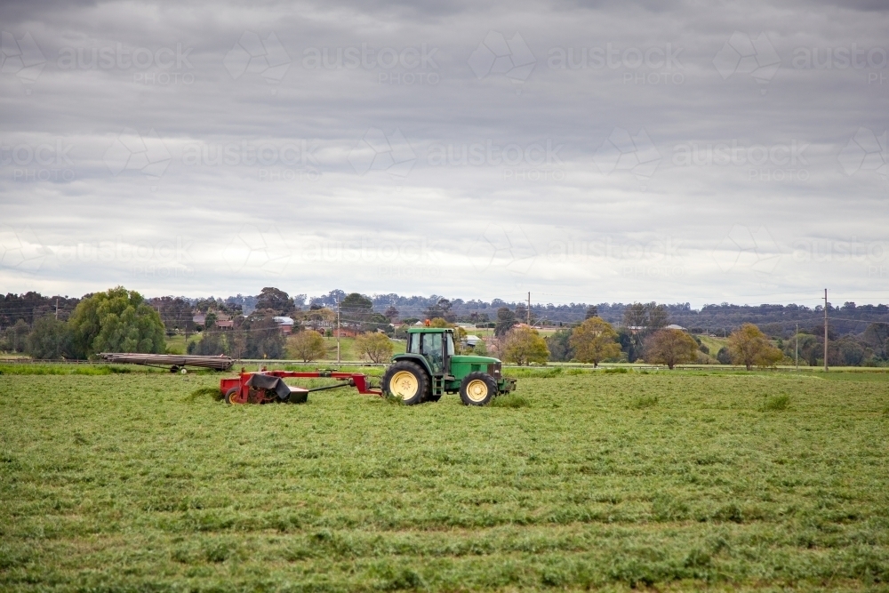 Green tractor pulling red slasher in lucerne paddock - Australian Stock Image