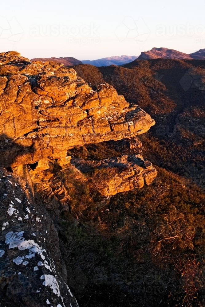 Cliff face in afternoon sun with mountains in background - Australian Stock Image