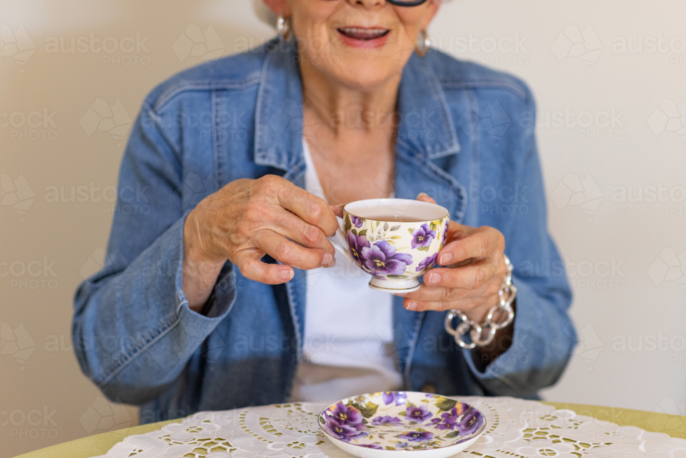 close image of elderly lady holding a cup of tea in a delicate floral china cup - Australian Stock Image