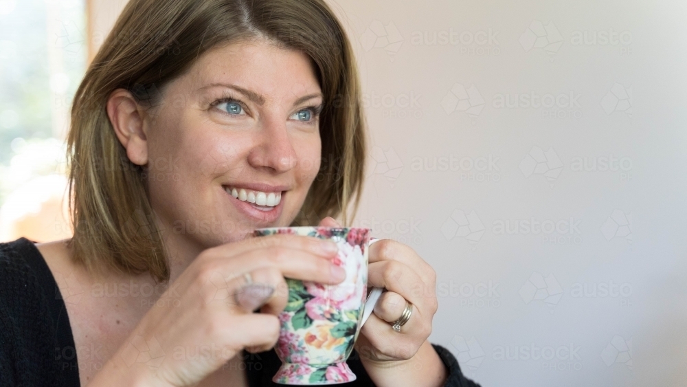 Close of young woman holding tea cup looking away from camera - Australian Stock Image