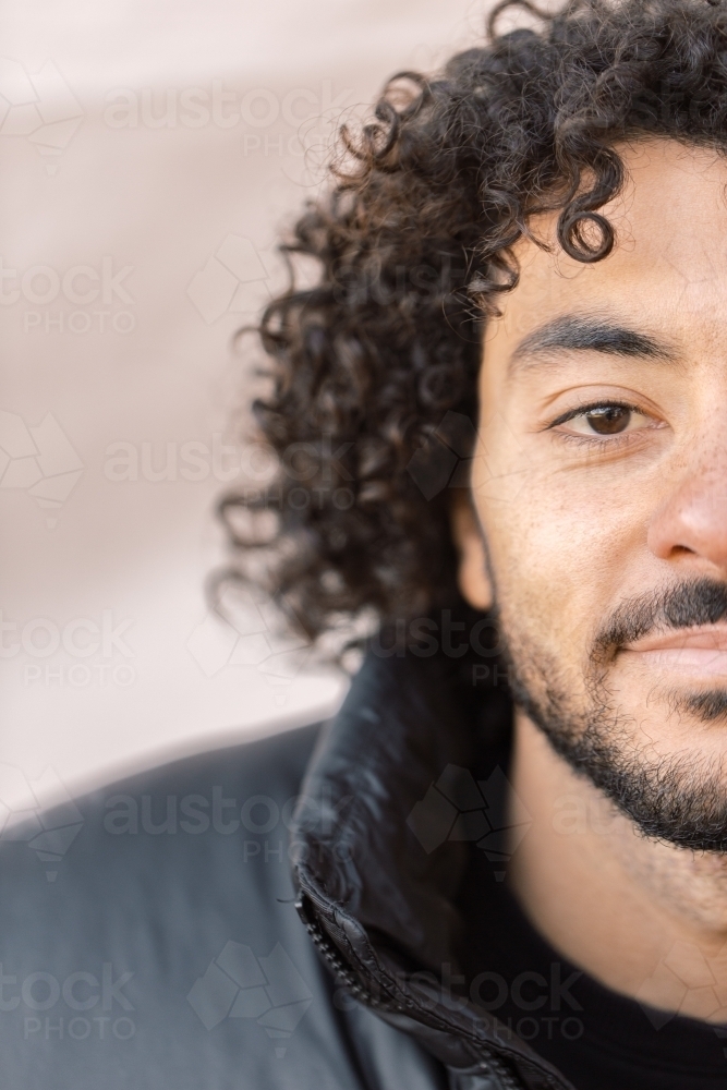 Close up and half face shot of a smiling young man with a curly hair and beard - Australian Stock Image