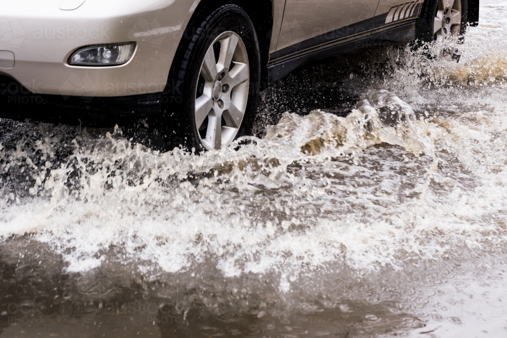 close up detail of an unrecognisable car travelling through dangerous flood water - Australian Stock Image