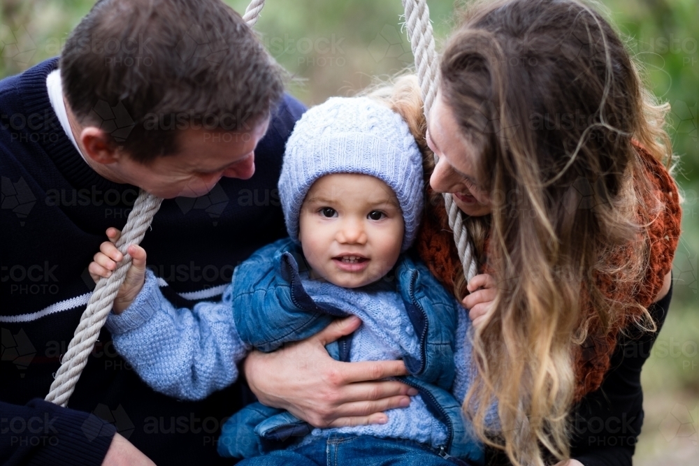 Close up Family portrait of mother father and with toddler on swing. - Australian Stock Image