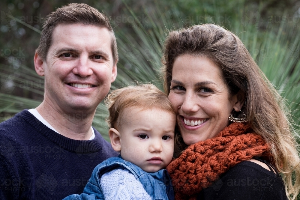 Close up Family portrait of three in bush setting looking at camera smiling - Australian Stock Image