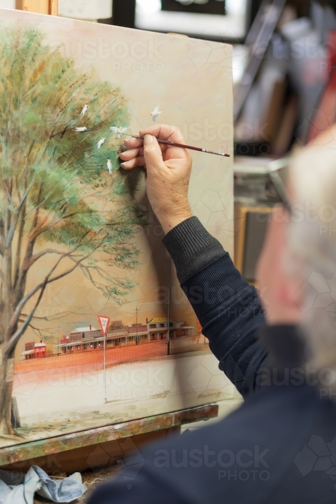 Close up looking over the shoulder of an artist painting a canvas - Australian Stock Image