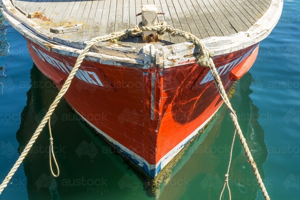 Close up of a boats bow reflecting in water and tied up with ropes - Australian Stock Image