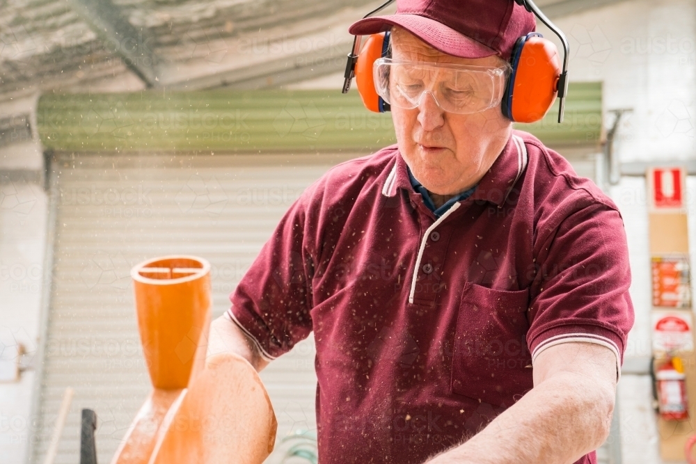 Close up of a elderly handyman wearing hearing protective and glasses working in a Men's shed - Australian Stock Image