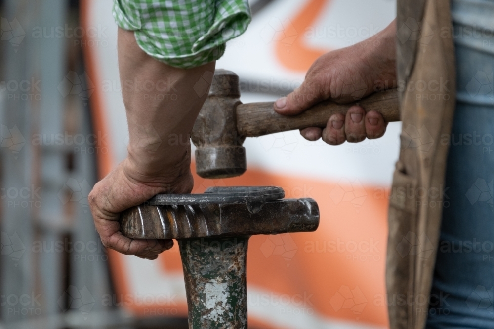 Close up of a farrier shaping a horse shoe with a hammer - Australian Stock Image