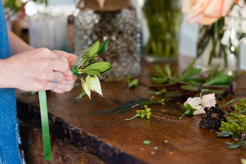 Close up of a florist preparing wedding buttonholes at a work bench - Australian Stock Image