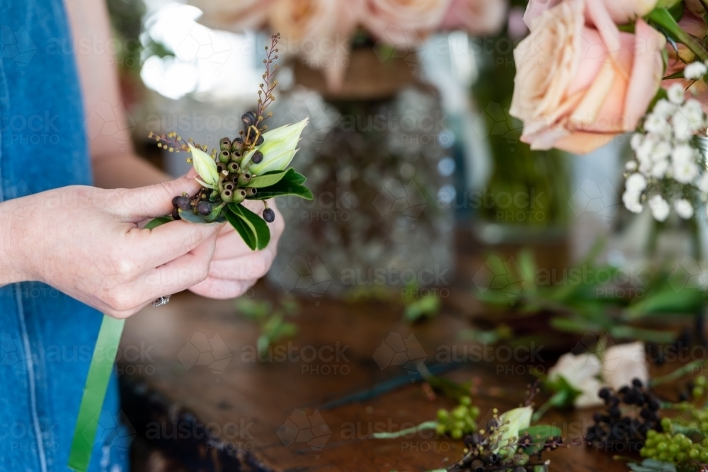 Close up of a florist preparing wedding buttonholes at a work bench - Australian Stock Image