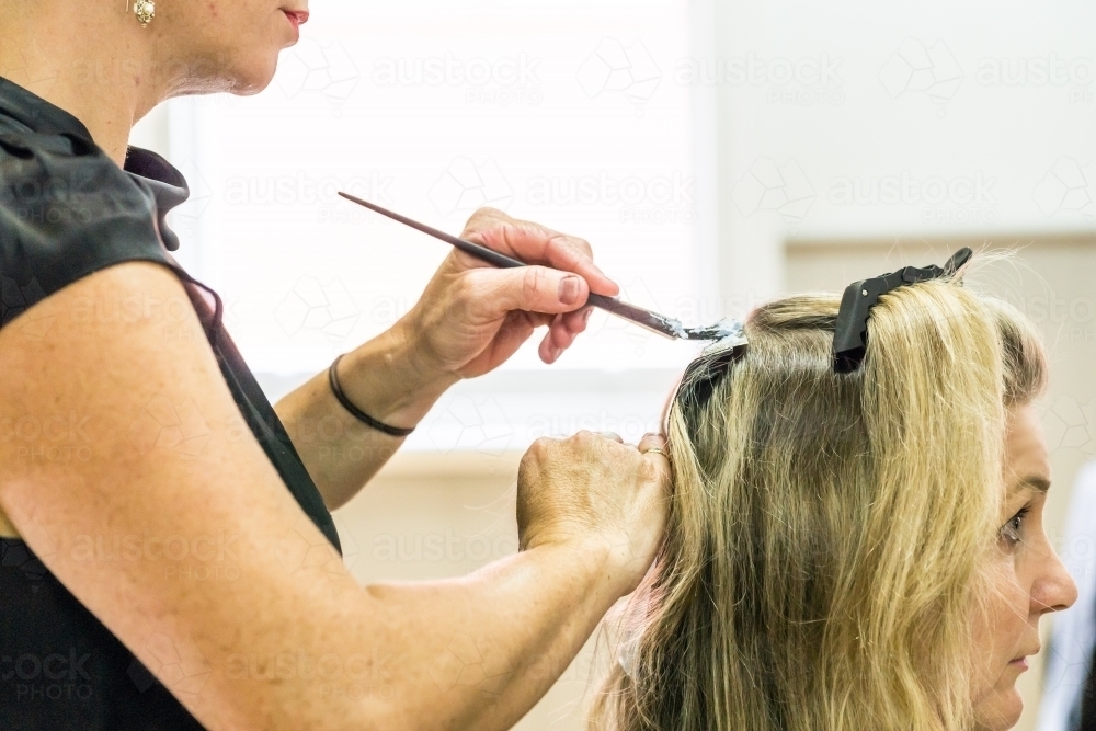 Close up of a hairdresser applying a treatment with a brush to a ladies hair - Australian Stock Image