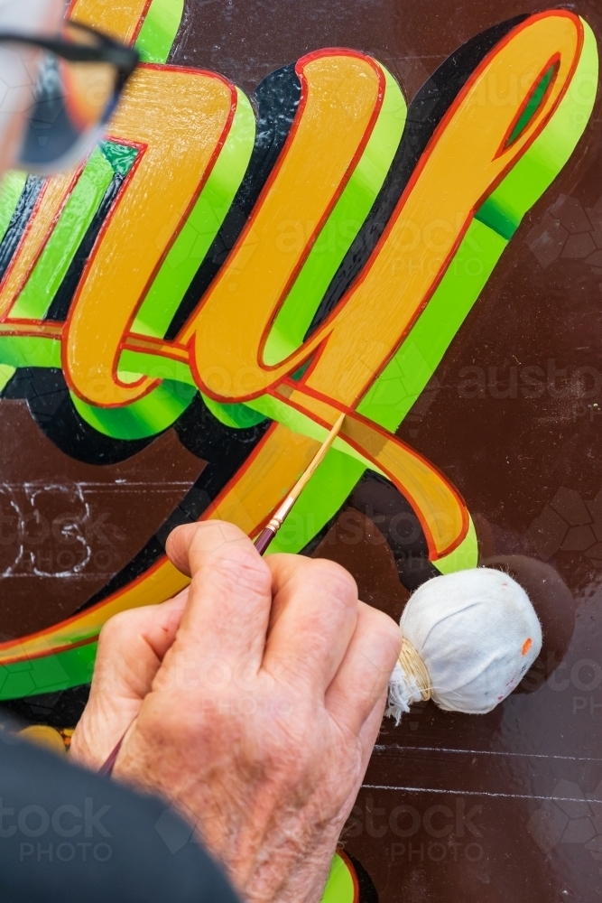 Close up of a hand painting in detailed lettering on a colourful sign - Australian Stock Image