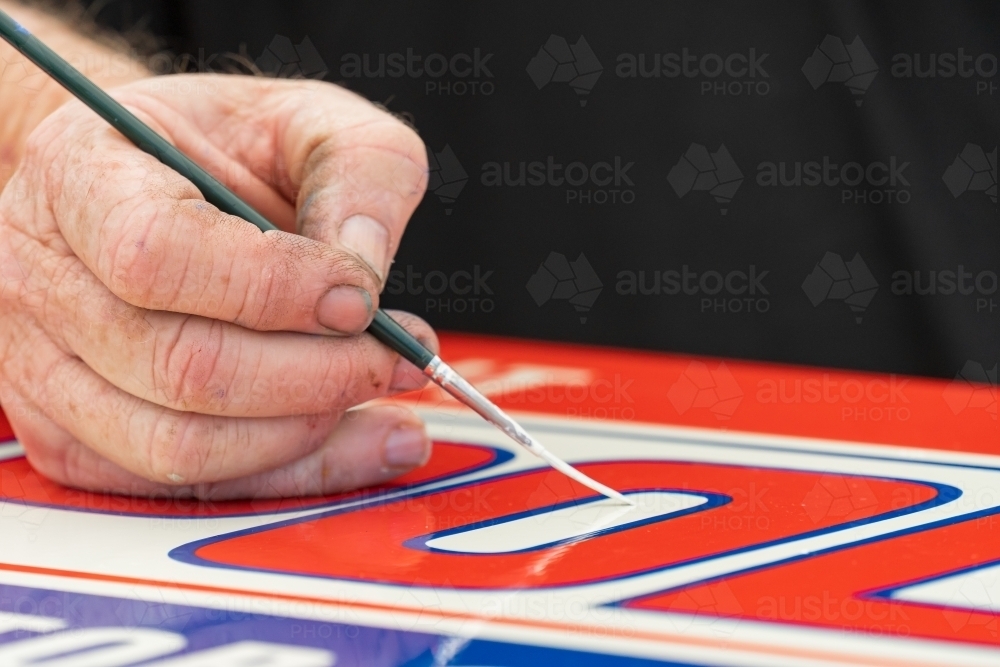 Close up of a hand painting in detailed lettering on a colourful sign - Australian Stock Image