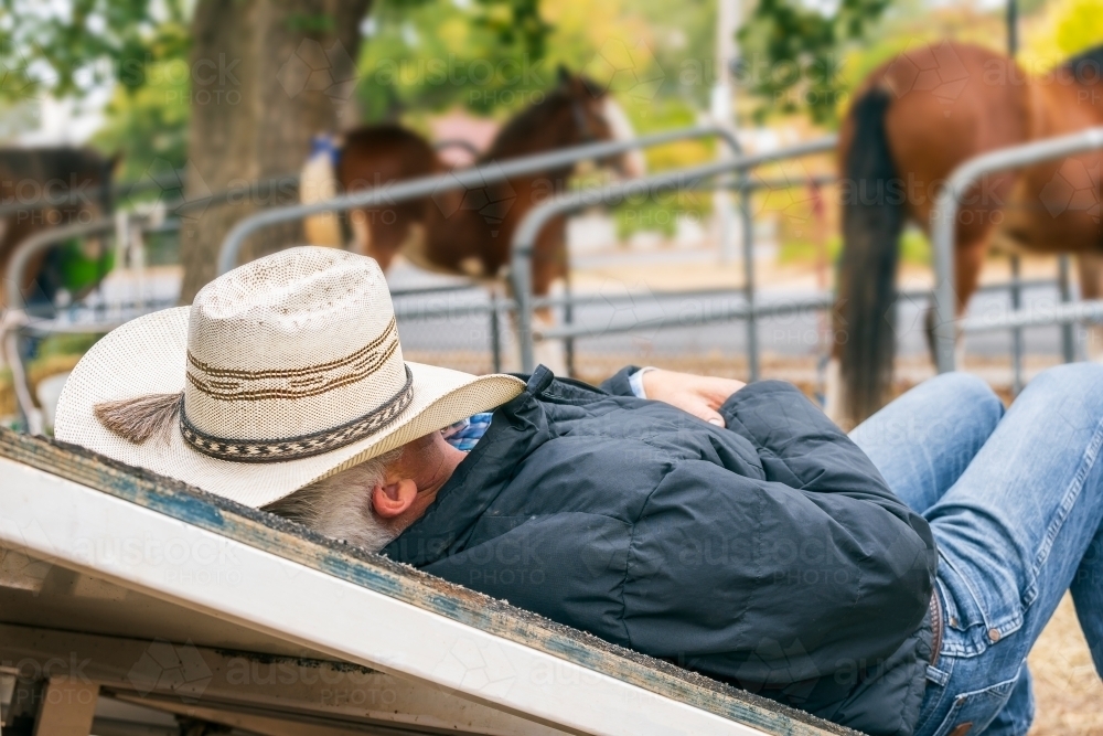 Close up of a horseman sleeping on a ramp with a cowboy hat over his face - Australian Stock Image