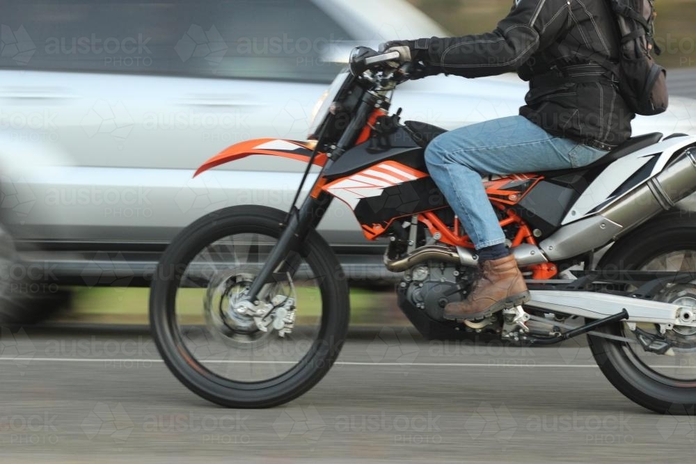 Close up of a man riding a motorbike past a car - Australian Stock Image
